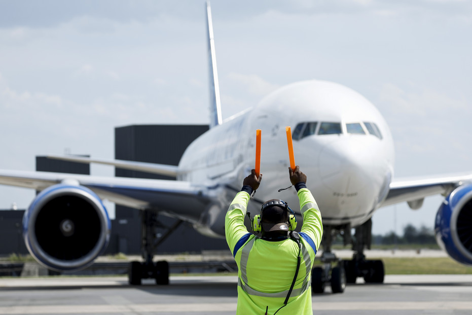 An airline worker guides a passenger plane at Dulles International Airport in June. The production of sustainable aviation fuel is increasing. 