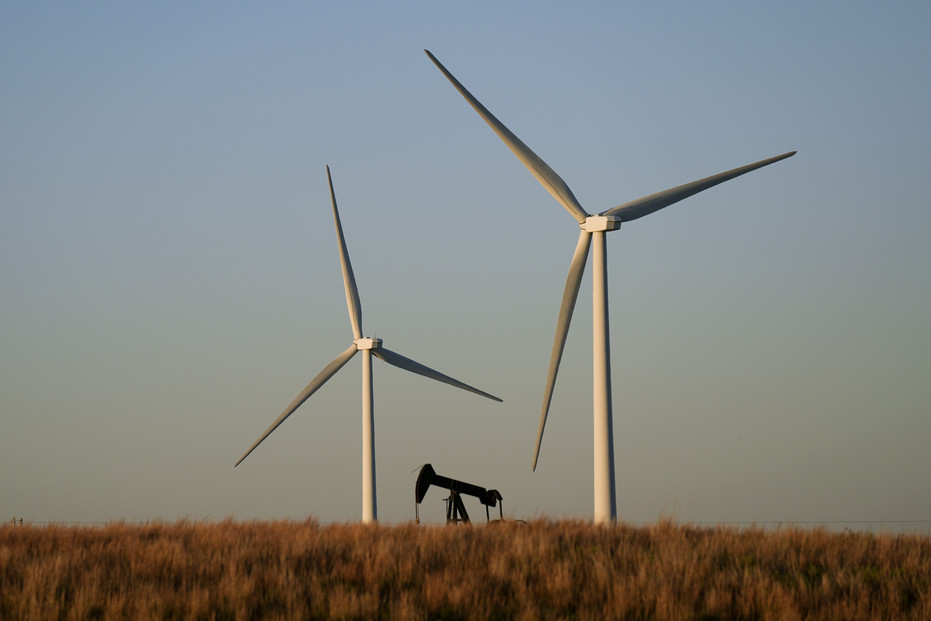An oil pumping unit works in the foreground while wind turbines at the Buckeye Wind Energy wind farm rise in the distance Sept. 30, 2024, near Hays, Kansas. An oil pumping unit works in the foreground while wind turbines at the Buckeye Wind Energy wind farm rise in the distance Sept. 30, 2024, near Hays, Kansas.